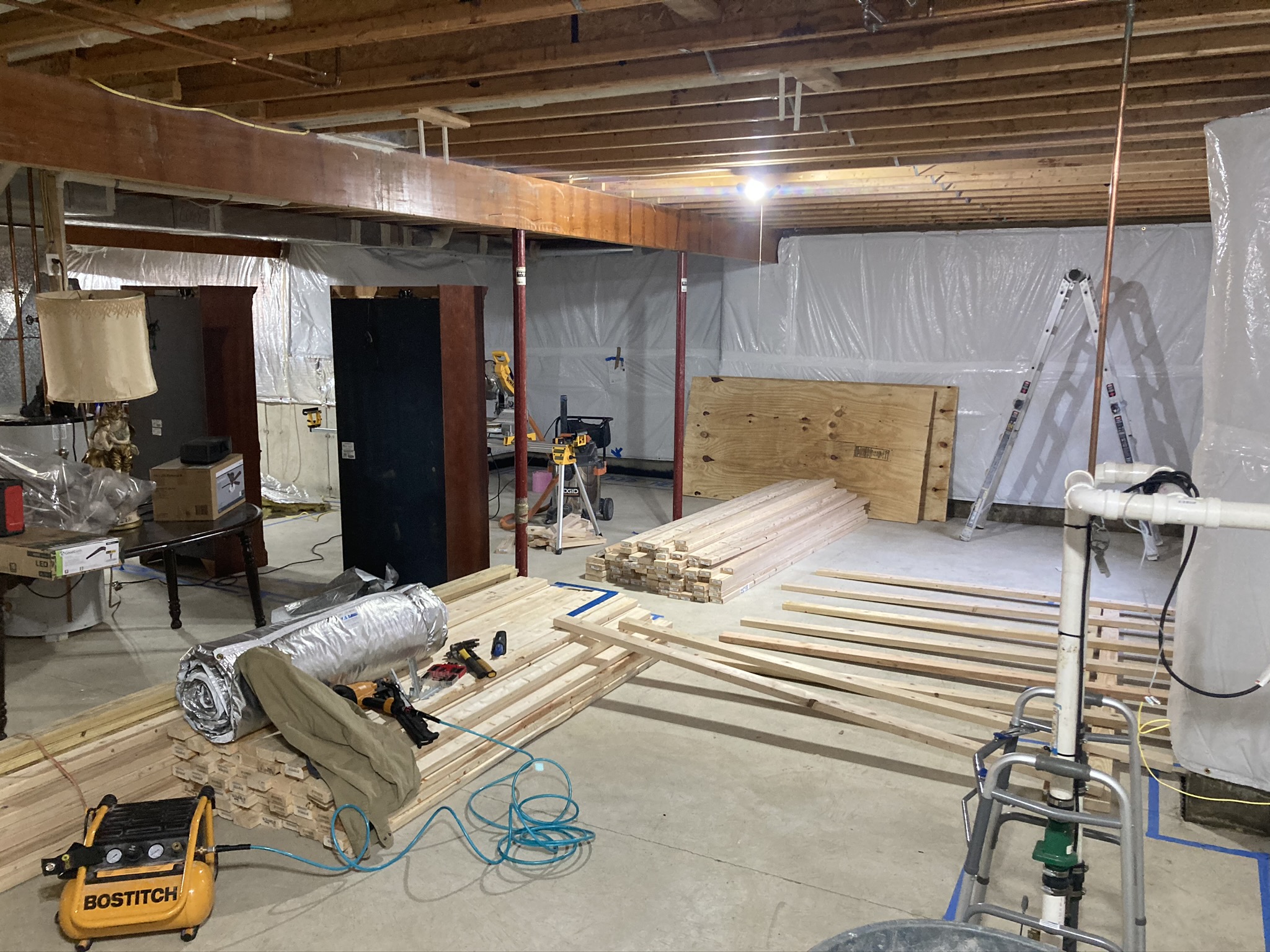 Basement reconstruction in progress with framing lumber, tools, and plastic containment