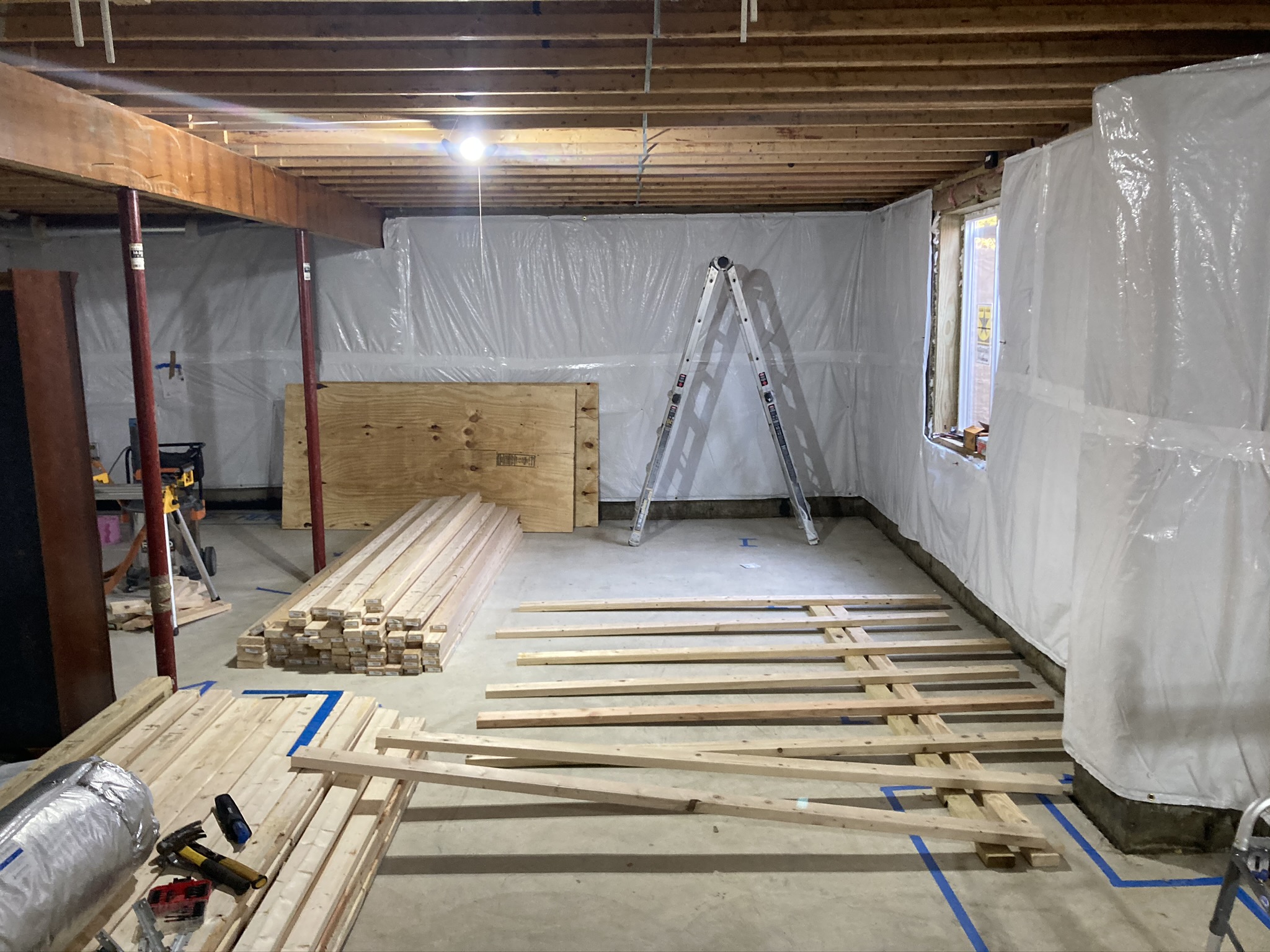 Basement rebuild with framing lumber laid out and plastic containment